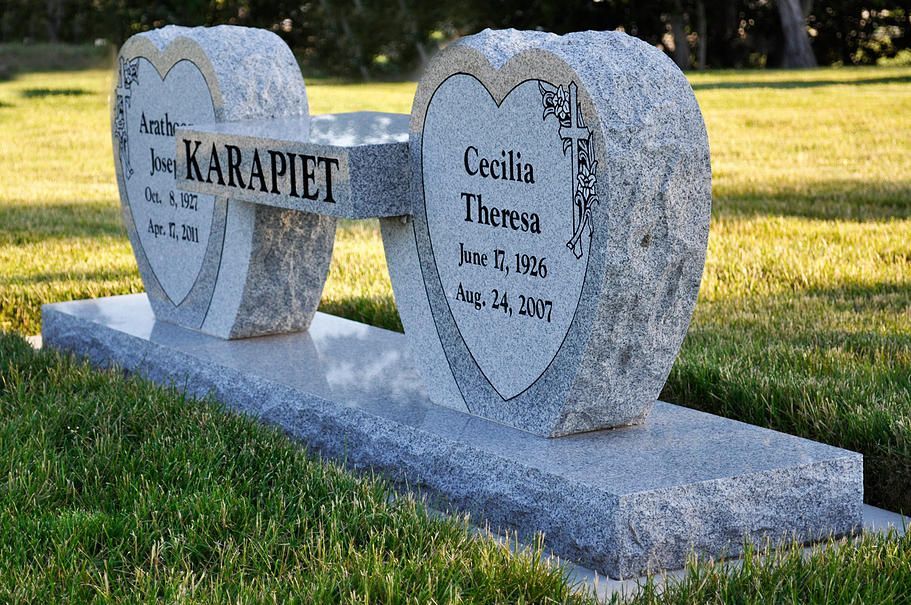Two heart-shaped granite headstones on a grave marker in a grassy cemetery.