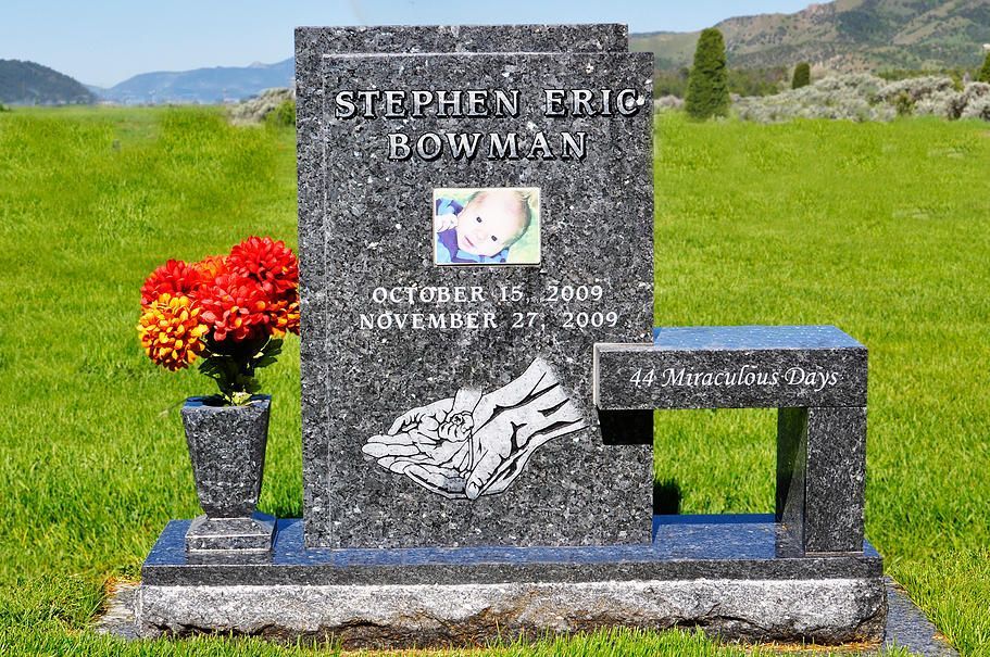 Gravestone with white flowers and red bouquet in a green cemetery, with mountains in the background