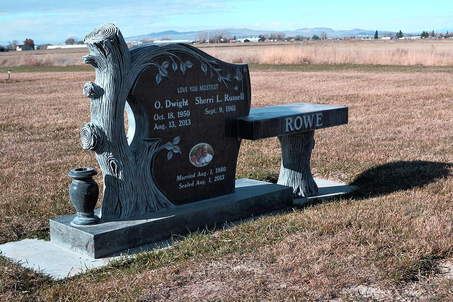 Black granite roadside memorial bench in a field, with engraved names and a small vase.