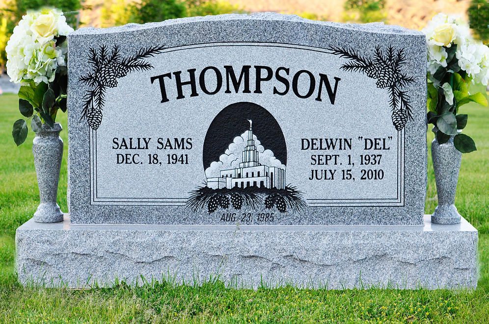 Gray Thompson gravestone with engraved names and dates, flanked by flower arrangements