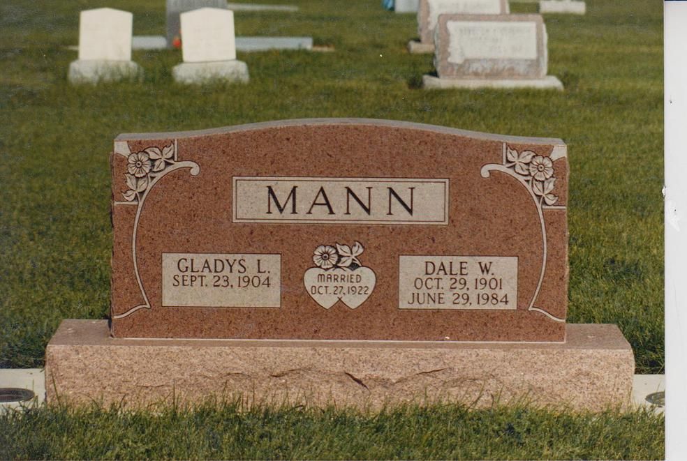 Mann family gravestone in a grassy cemetery, with two name plaques and small floral engraving.