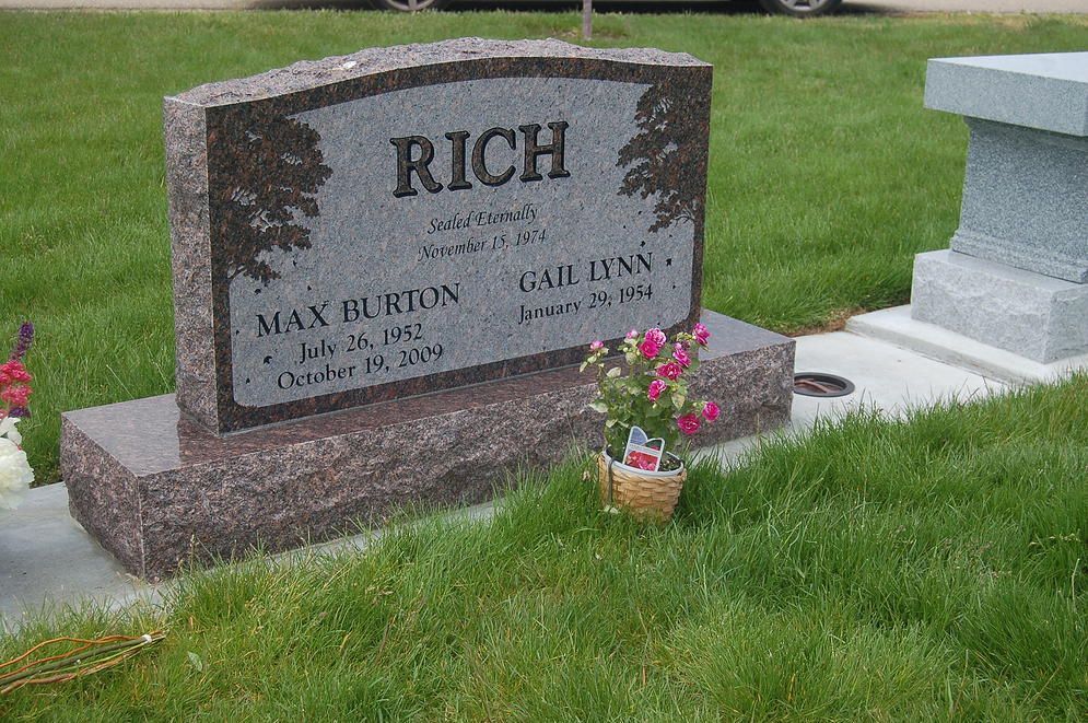 Granite gravestone in a grassy cemetery with pink flowers at the base and the name “RICH” engraved.
