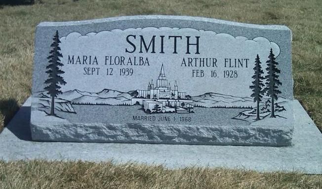 Gray engraved gravestone in a grassy cemetery with trees and a church scene, labeled Smith, Maria Floralba, and Arthur Flint