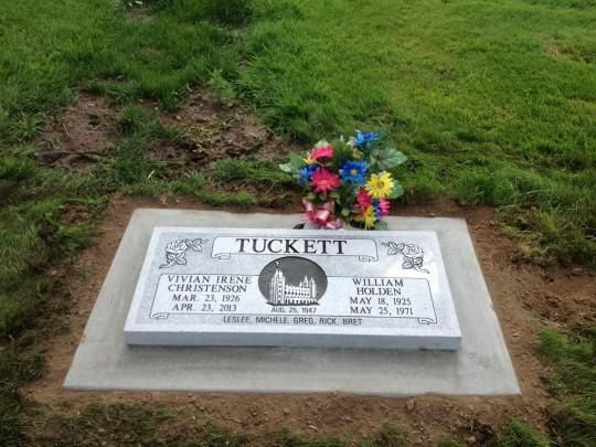Gravestone marked “TUCKETT” with colorful flowers on a grassy plot.