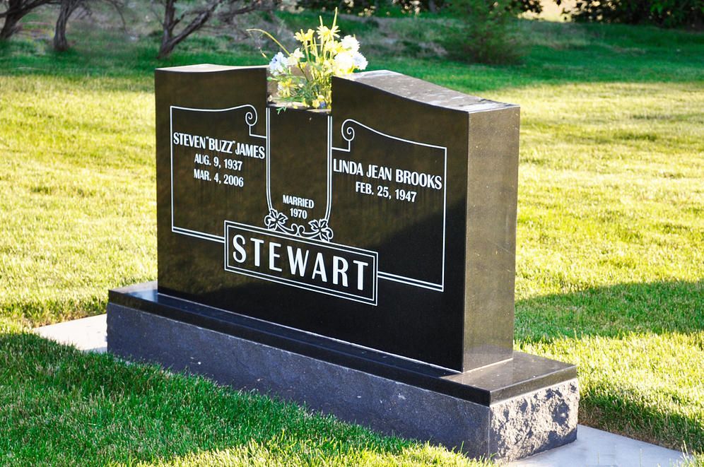 Black granite gravestone with flowers on a grassy lawn, engraved with the Stewart name.