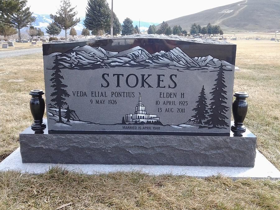 Black granite memorial headstone reading “STOKES” in a grassy cemetery with mountains in the background