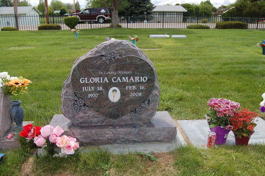 Gravestone in a grassy cemetery with bouquets of pink, red, and white flowers surrounding it