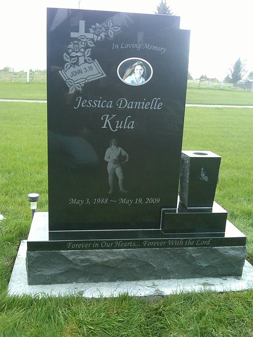 Black memorial gravestone with engraved portrait in a grassy cemetery