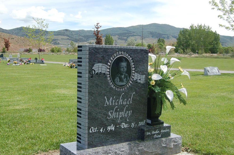 Gravestone with white flowers in a grassy cemetery, with hills in the background.
