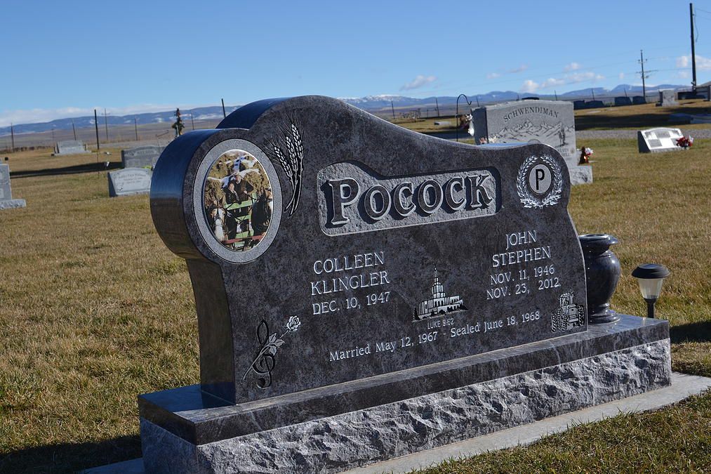 Black granite gravestone with carved lettering in a cemetery under a clear sky.