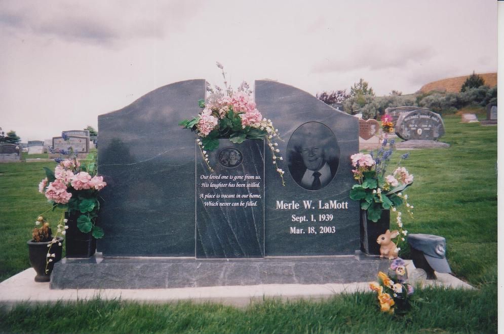 Dark granite cemetery headstone with pink flowers on a grassy lawn