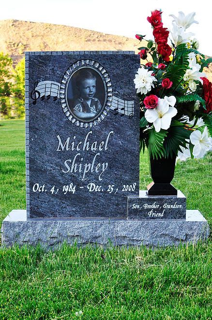 Gravestone with portrait, engraved name and dates, beside a black vase of red and white flowers.