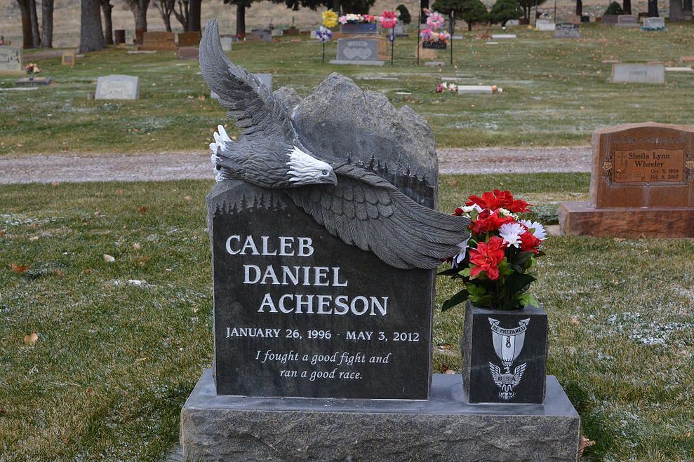 Gravestone for Caleb Daniel Acheson with a large eagle sculpture and red flowers in a cemetery