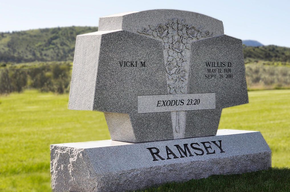 Granite memorial marker in a grassy field with engraved names and Bible verses, including “RAMSEY” on the base