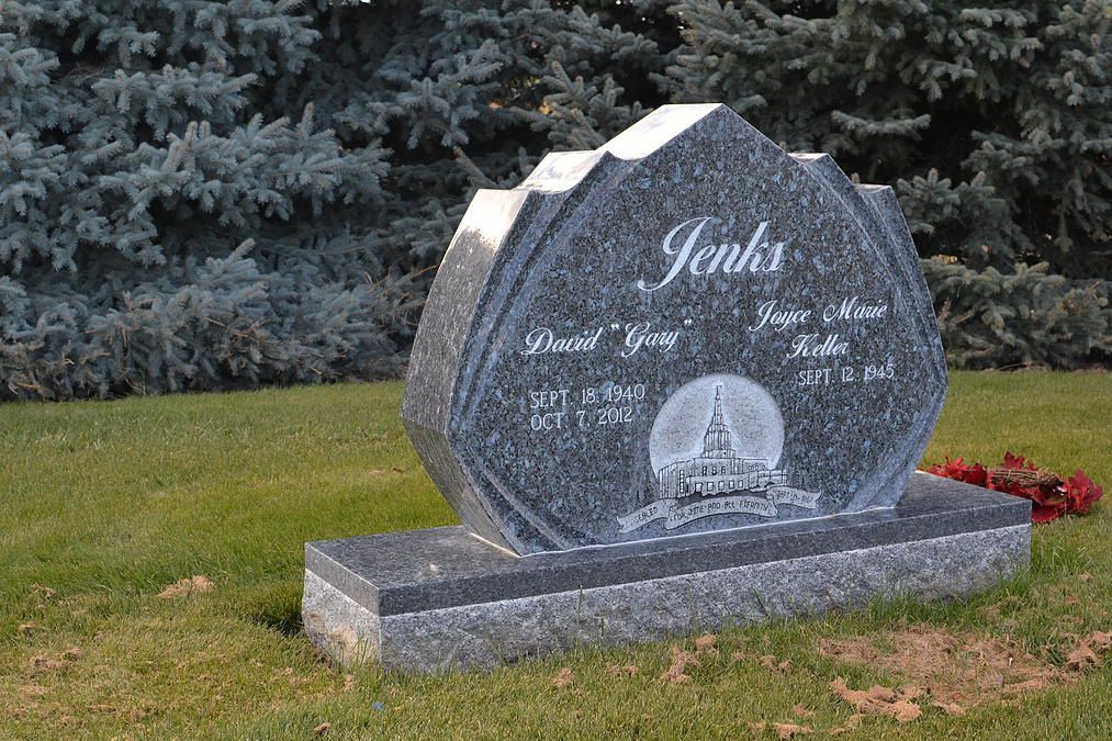 Gray granite gravestone with engraved name “Jenkins” on a grassy lawn by evergreen trees