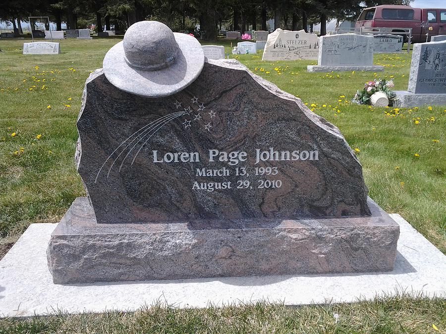 Gravestone for Loren Page Johnson with a hat resting on top, in a cemetery