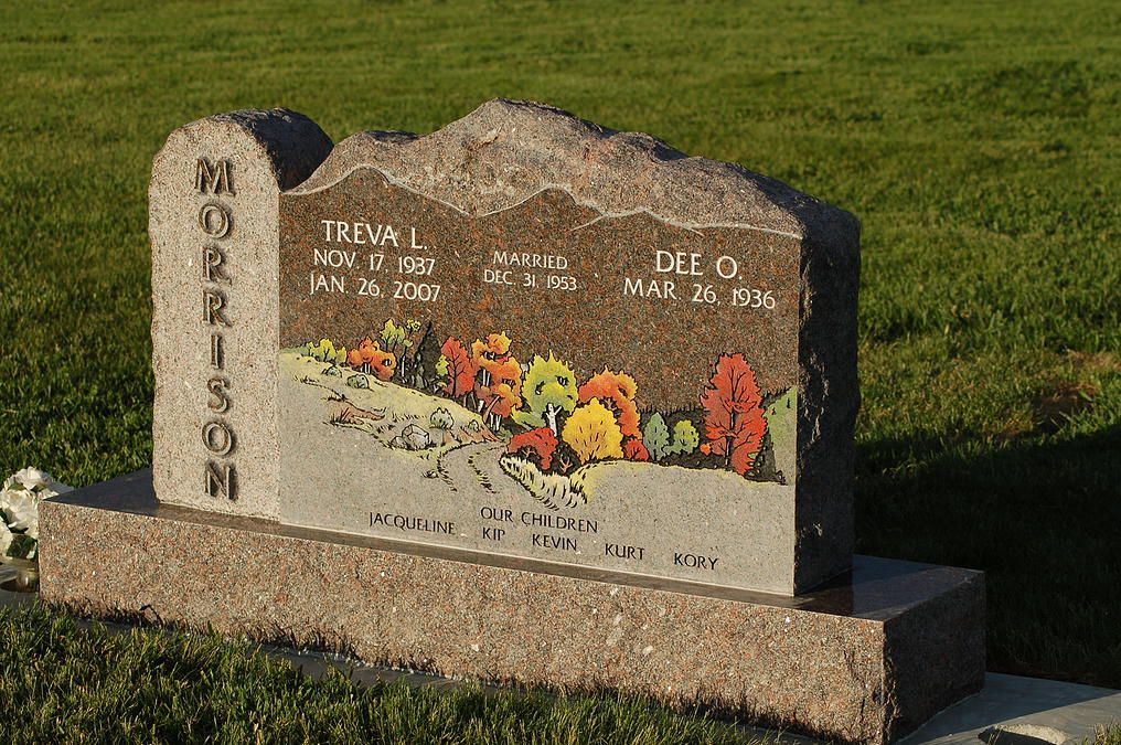 Memorial stone with engraved names and painted flowers on a grassy lawn