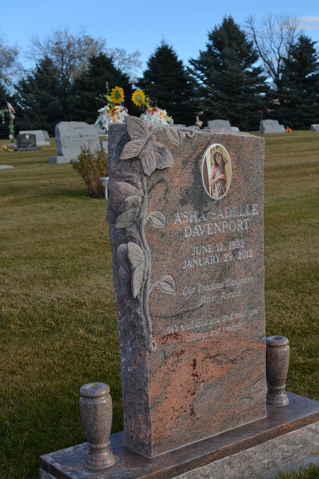 Polished pink granite gravestone with flowers in a cemetery on a grassy hill