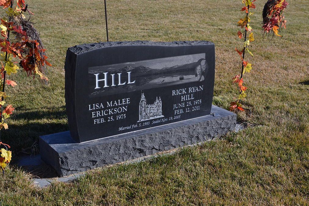 Black granite gravestone on grass with autumn floral decorations, engraved with the name HILL.