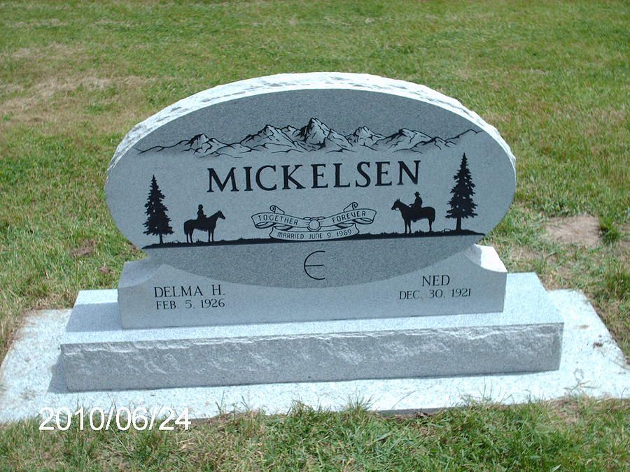 Gray gravestone marked “MICKELSEN” with tree and mountain engraving on a grassy cemetery plot.