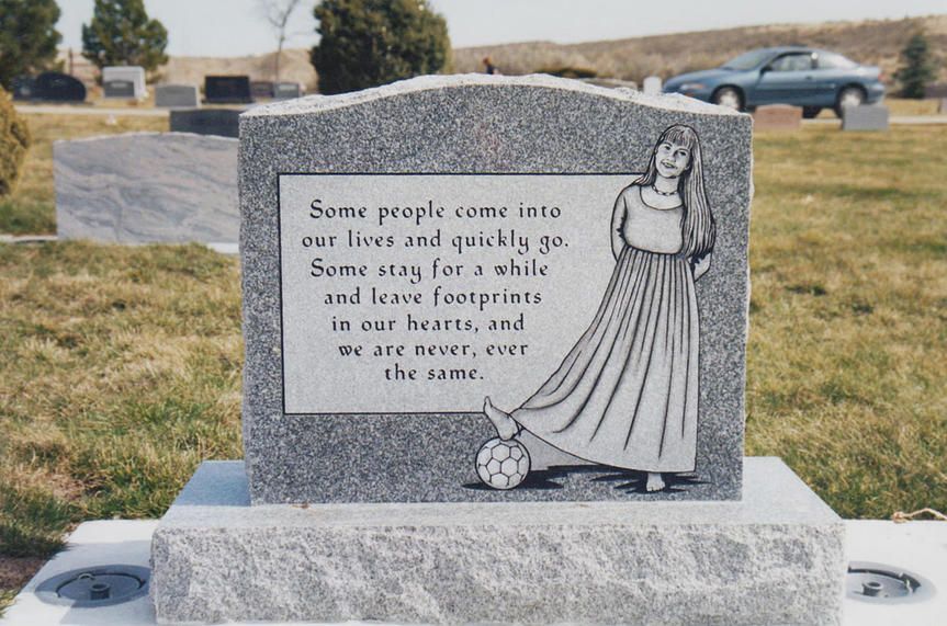 Gravestone with engraved poem and a child figure in a cemetery, with grass and cars in the background