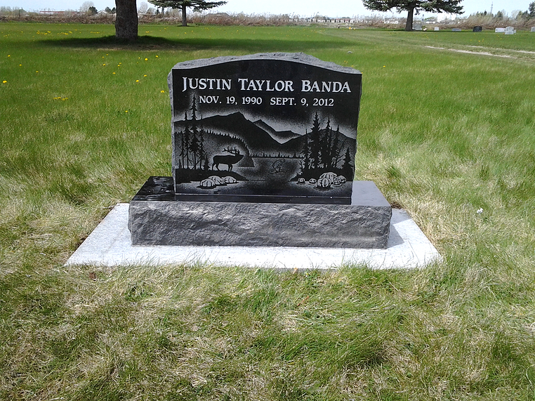Black granite memorial gravestone on a grassy lawn with trees in the background.