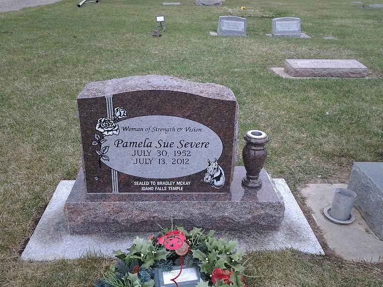 Gravestone with flower vase in a cemetery, surrounded by grass and other headstones.