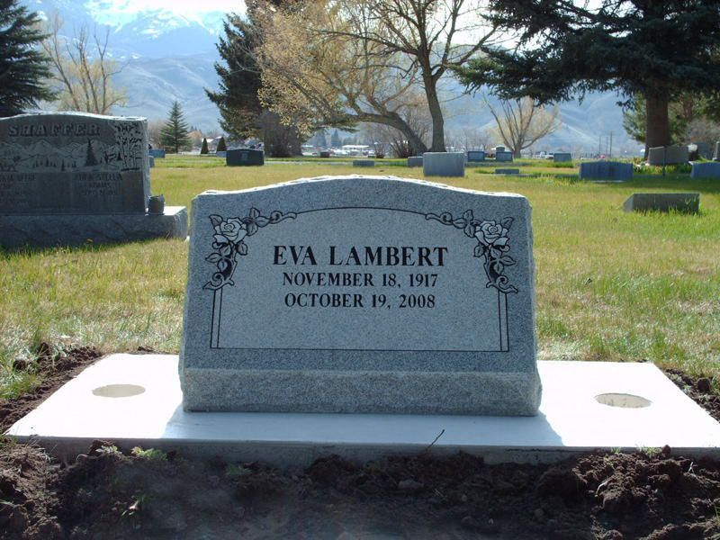 Gray gravestone for Eva Lambert in a sunny cemetery with mountains in the background.