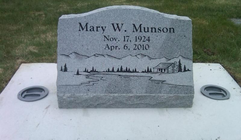 Gray gravestone for Mary W. Munson with carved waterfront scene and dates, on a white memorial base