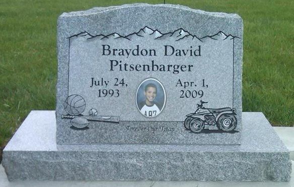 Gray granite gravestone with carved name, dates, oval photo, and motorcycle engraving in a grassy cemetery