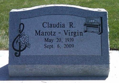 Gray granite gravestone with engraved name, dates, treble clef, and trumpet in a cemetery