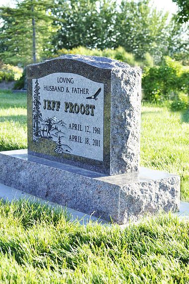 Gray engraved memorial stone in a grassy field with trees in the background