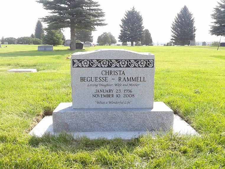 Gravestone in a sunny cemetery lawn with trees in the background
