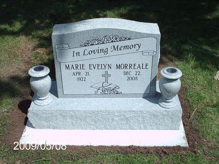White marble gravestone with vase ornaments on a grassy lawn, engraved “In Loving Memory” and “Marie Evelyn Morriale.”