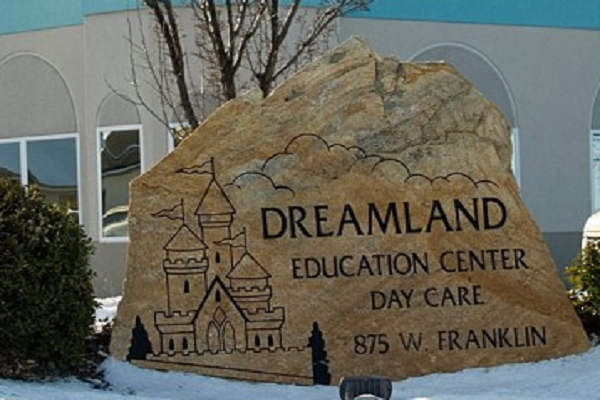 Stone sign for Dreamland Education Center Day Care in front of a building, with castle artwork and snow.