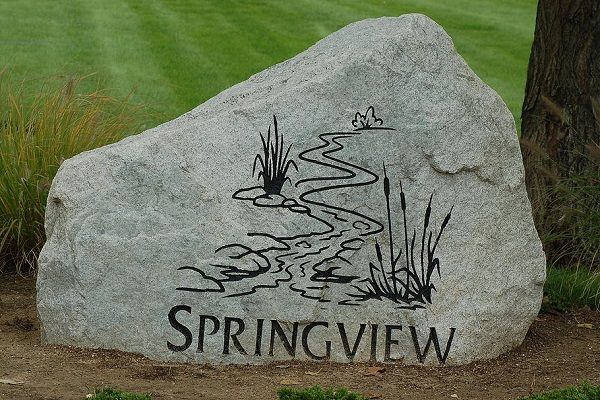 Springview engraved on a large gray stone beside a grassy landscape