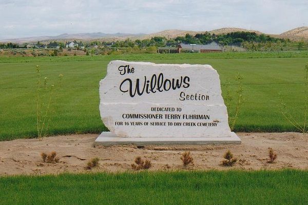 White stone entrance sign reading “The Willows,” set in a grassy field with hills in the background.