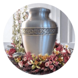 Silver funeral urn surrounded by pink and red flowers in a bright memorial setting