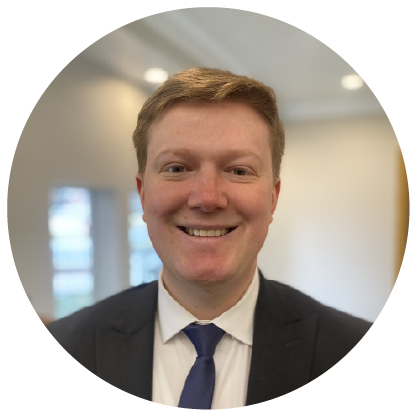 Smiling person in a dark suit and blue tie in a bright office hallway