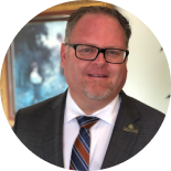 Smiling man in glasses and a suit with a striped tie, posed in a circular portrait background
