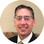 Smiling man in glasses and suit jacket against a light background