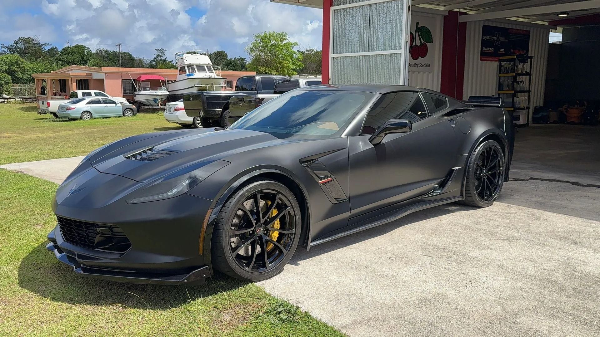 A matte black Chevrolet Corvette Z06 parked on a paved driveway next to a building on a sunny day.
