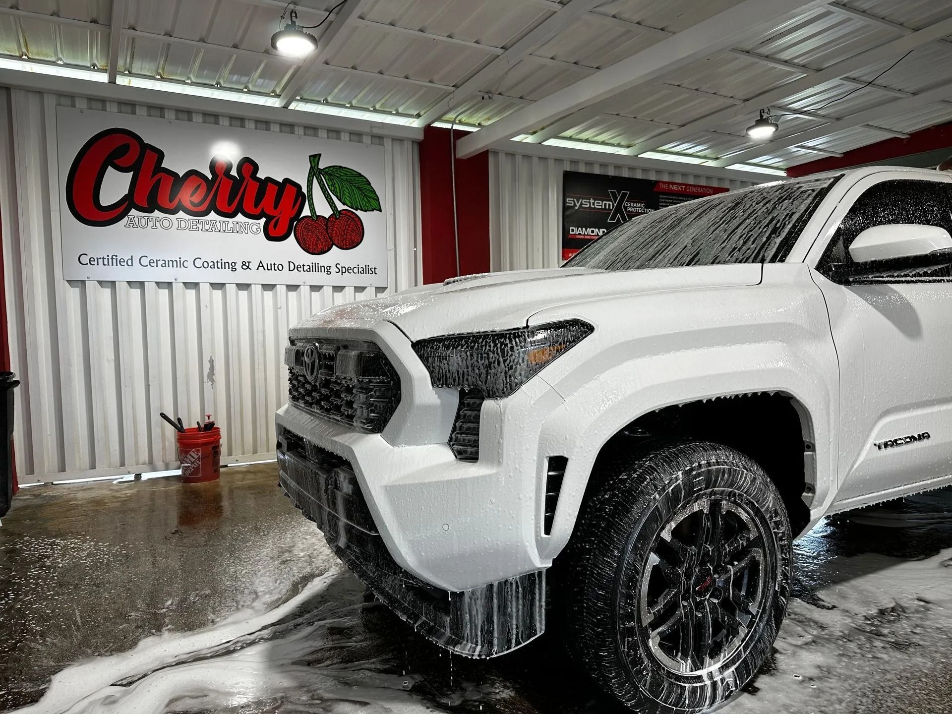 A white truck covered in thick soap suds parked at a car wash branded with a