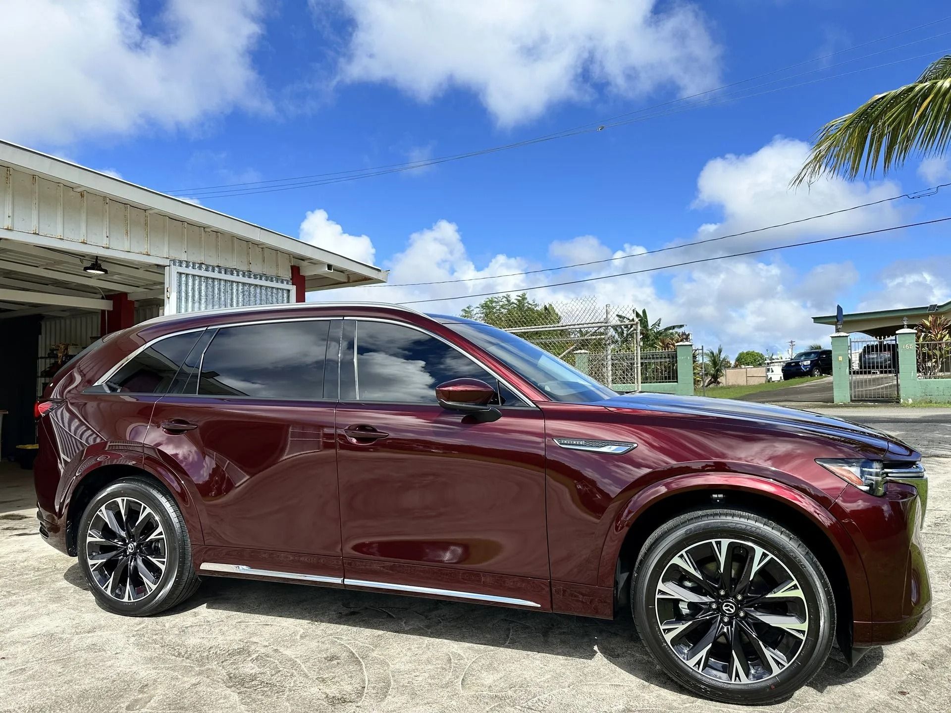 A dark red Mazda CX-90 SUV parked outside on a sunny day with a blue sky.