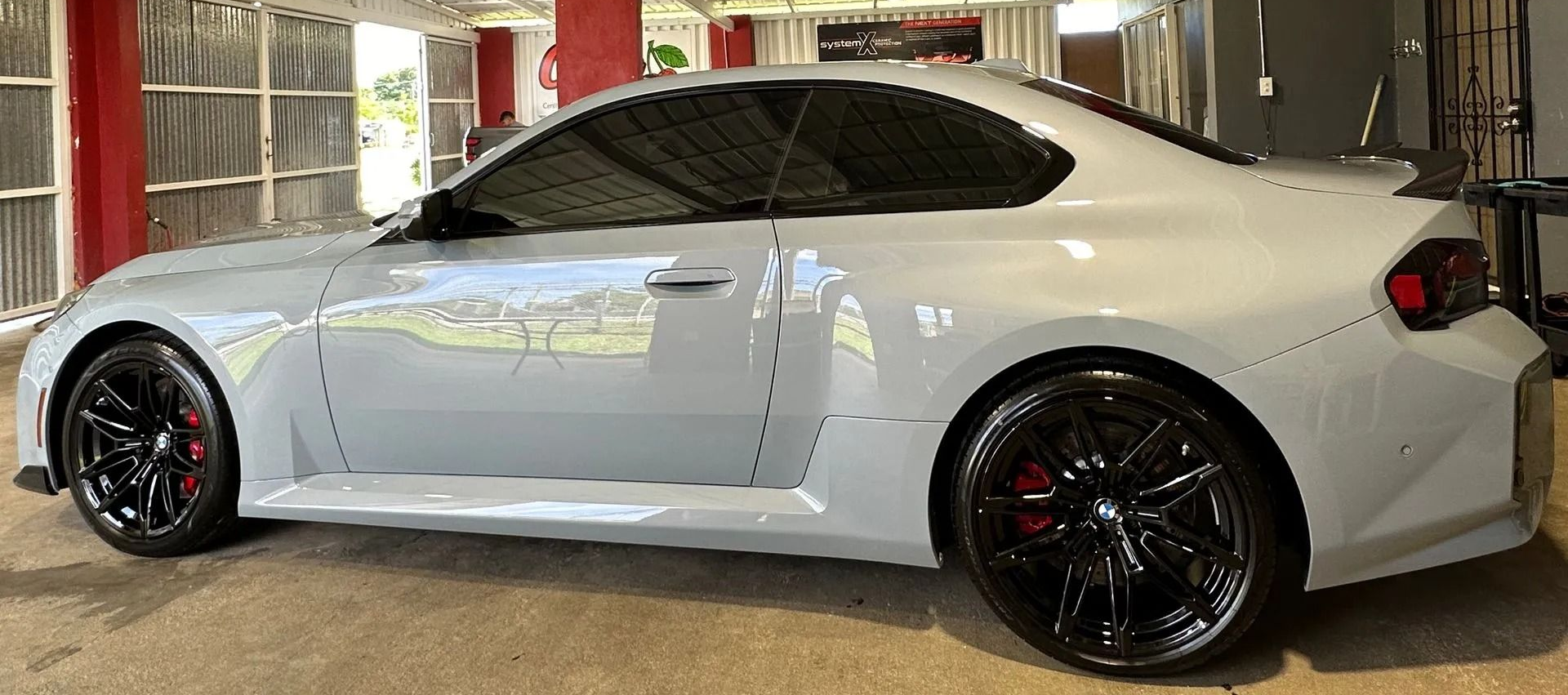 Side view of a light gray two-door sports car with black rims and red brake calipers, parked in a covered garage.