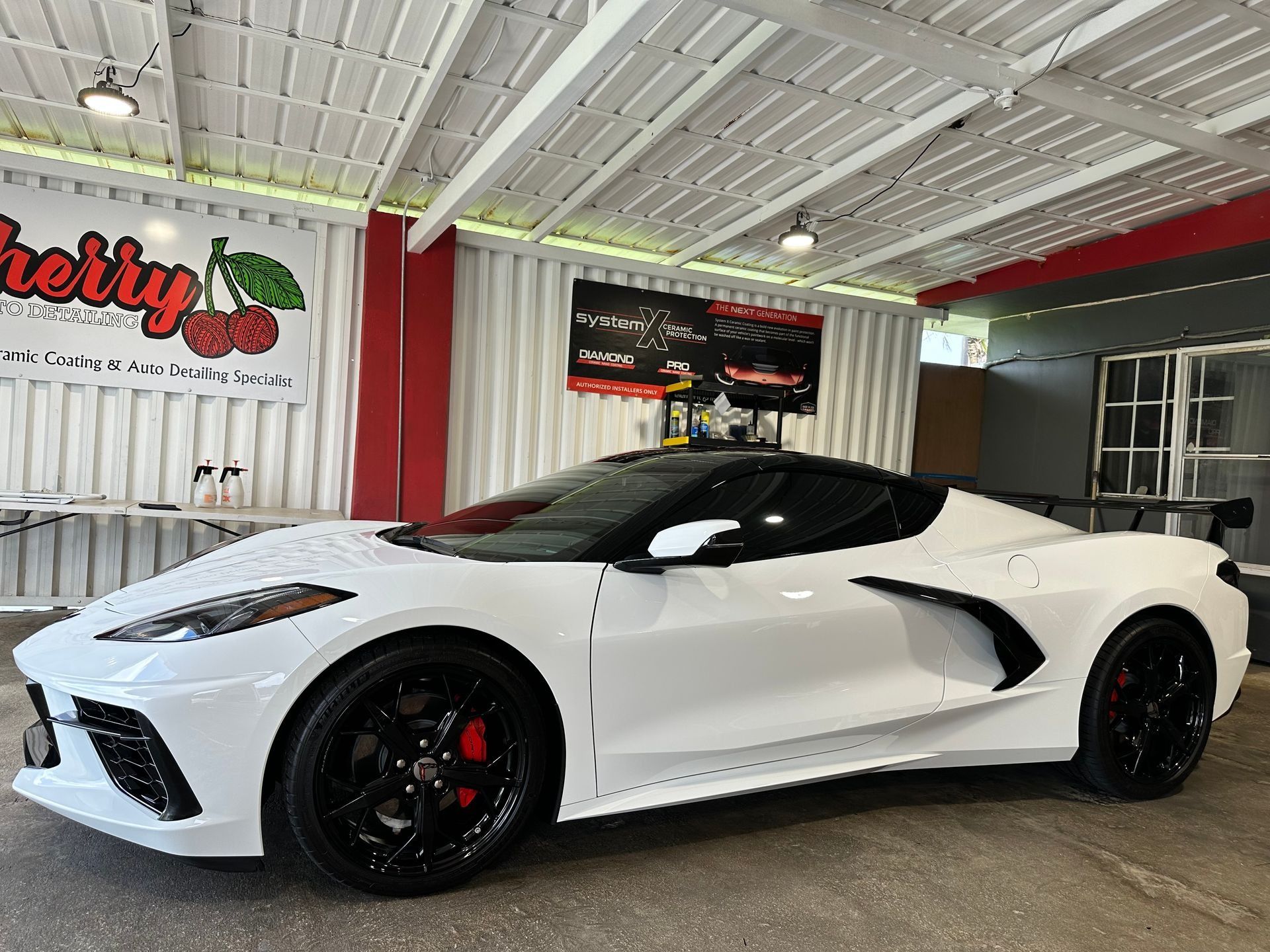 A white C8 Chevrolet Corvette parked inside a showroom with black wheels and red brake calipers.