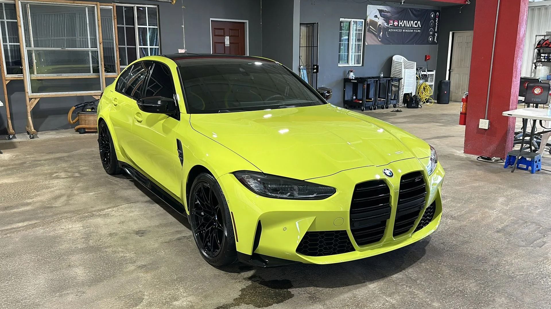 A lime-green BMW M3 sedan with a black roof and black wheels parked in an indoor garage.