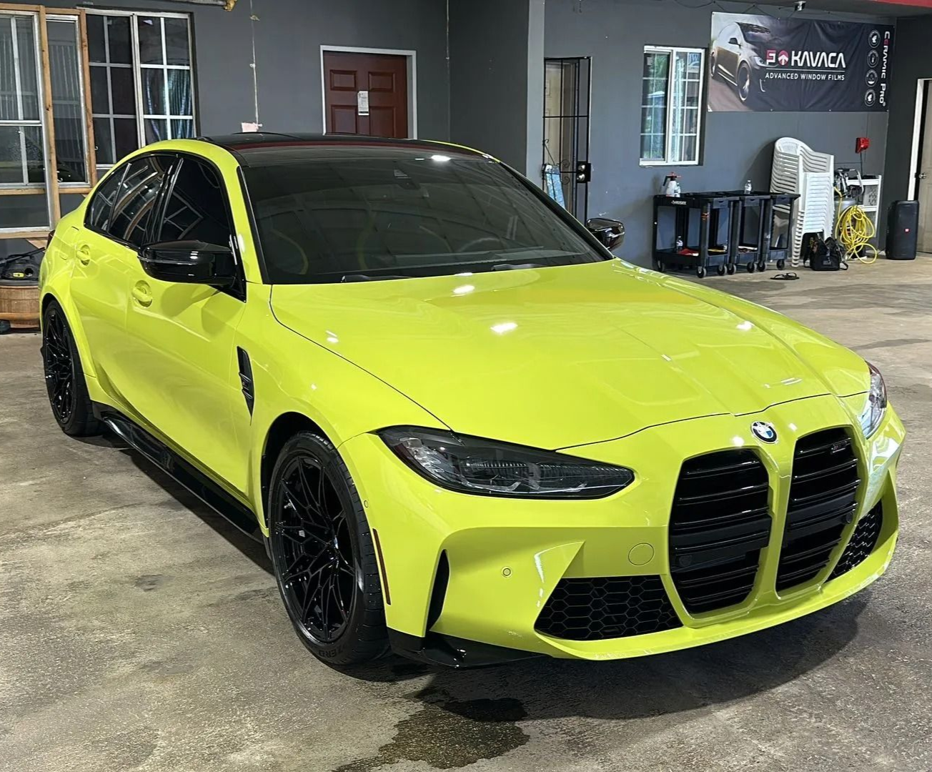 A lime green BMW M3 sedan parked inside a garage with black rims, a black roof, and black grille accents.