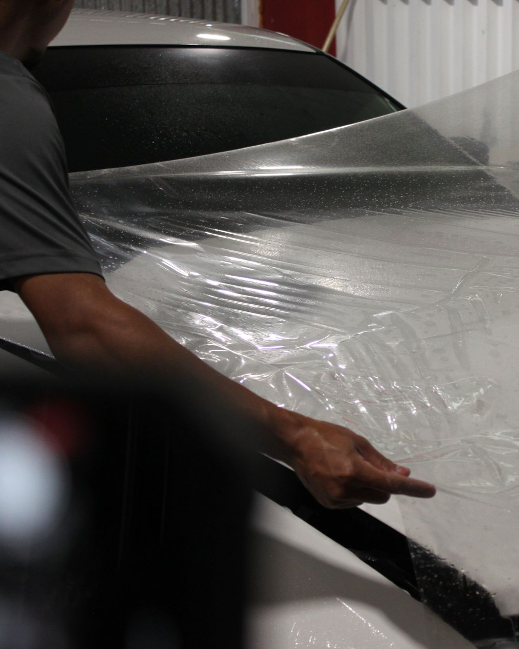 A person applying a clear protective film onto the white hood of a car.