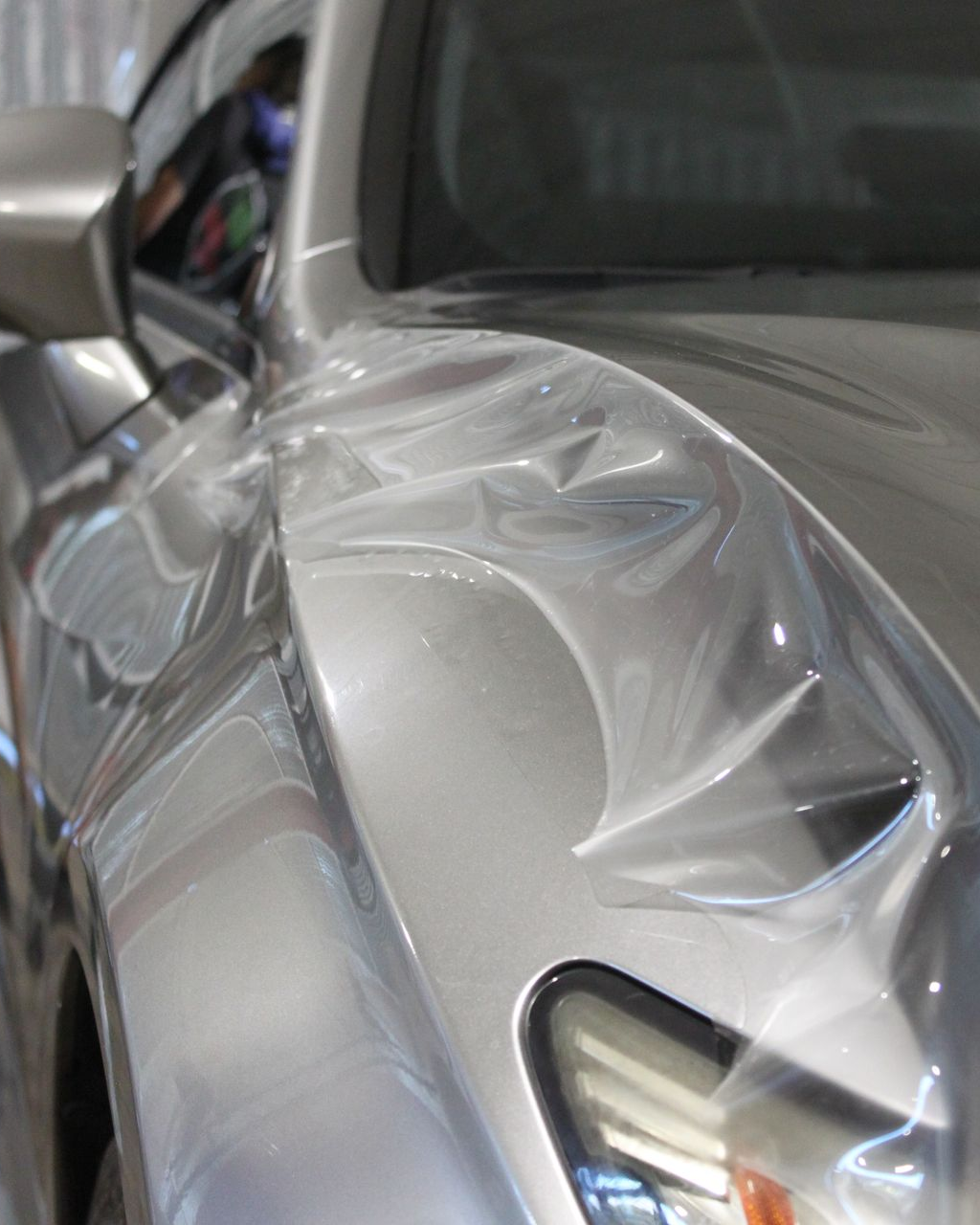Clear protective film being applied to the silver fender of a car.